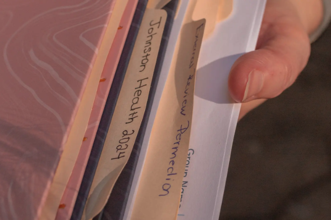 Person holds a stack of medical records in various folders in their hand.