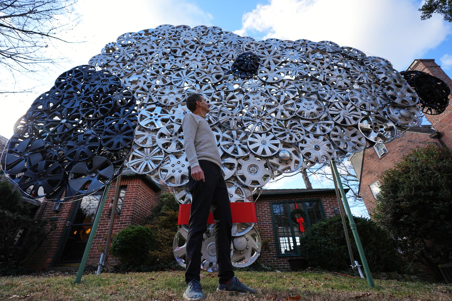 Cyclist Barnaby Wickham poses for a portrait in front of his art structure made from hubcaps, Dec. 11, 2025, at his home in Baltimore. (AP Photo/Stephanie Scarbrough)