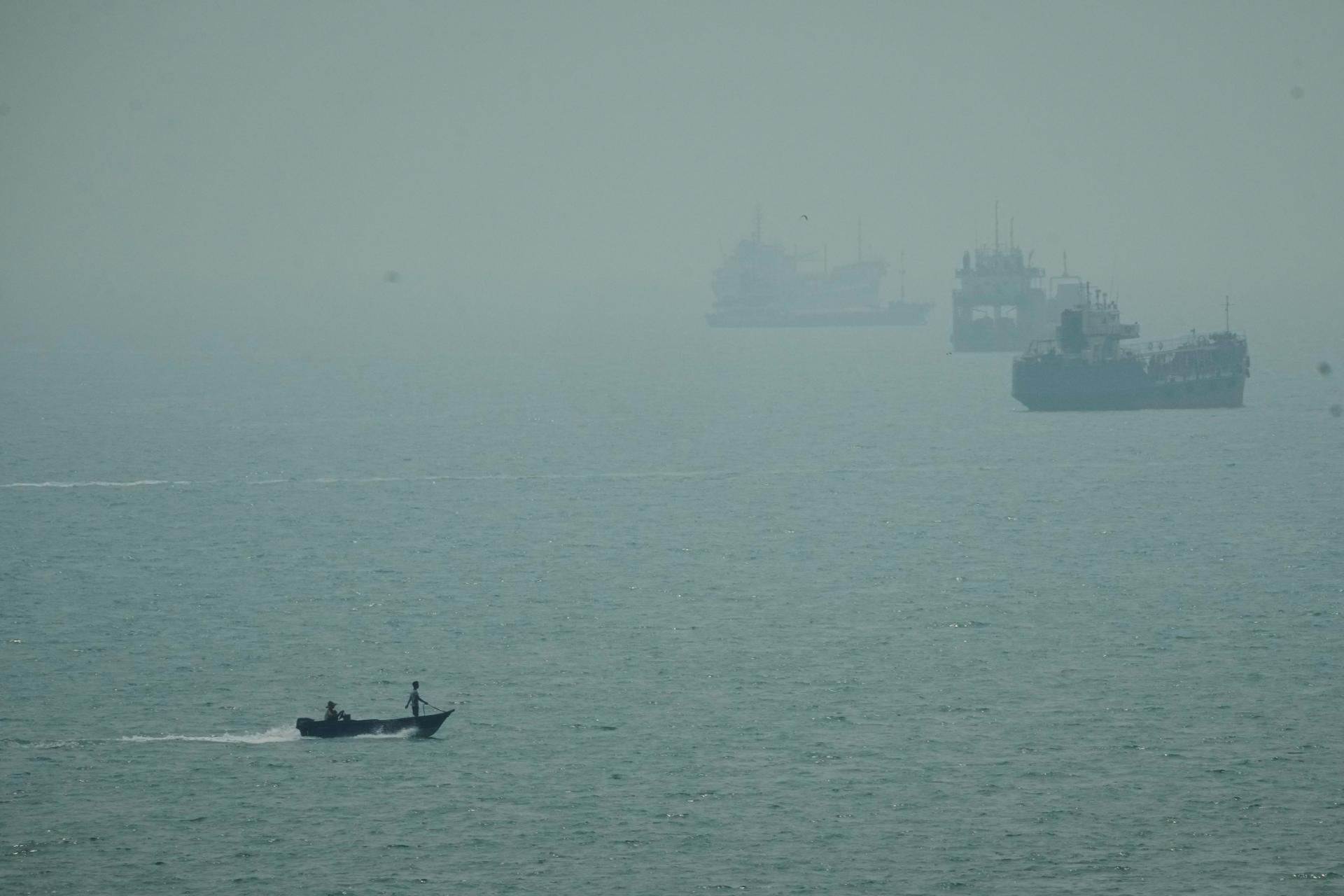 A motorboat travels past commercial vessels anchored amid haze in the Strait of Hormuz off Bandar Abbas, Iran, Monday. 