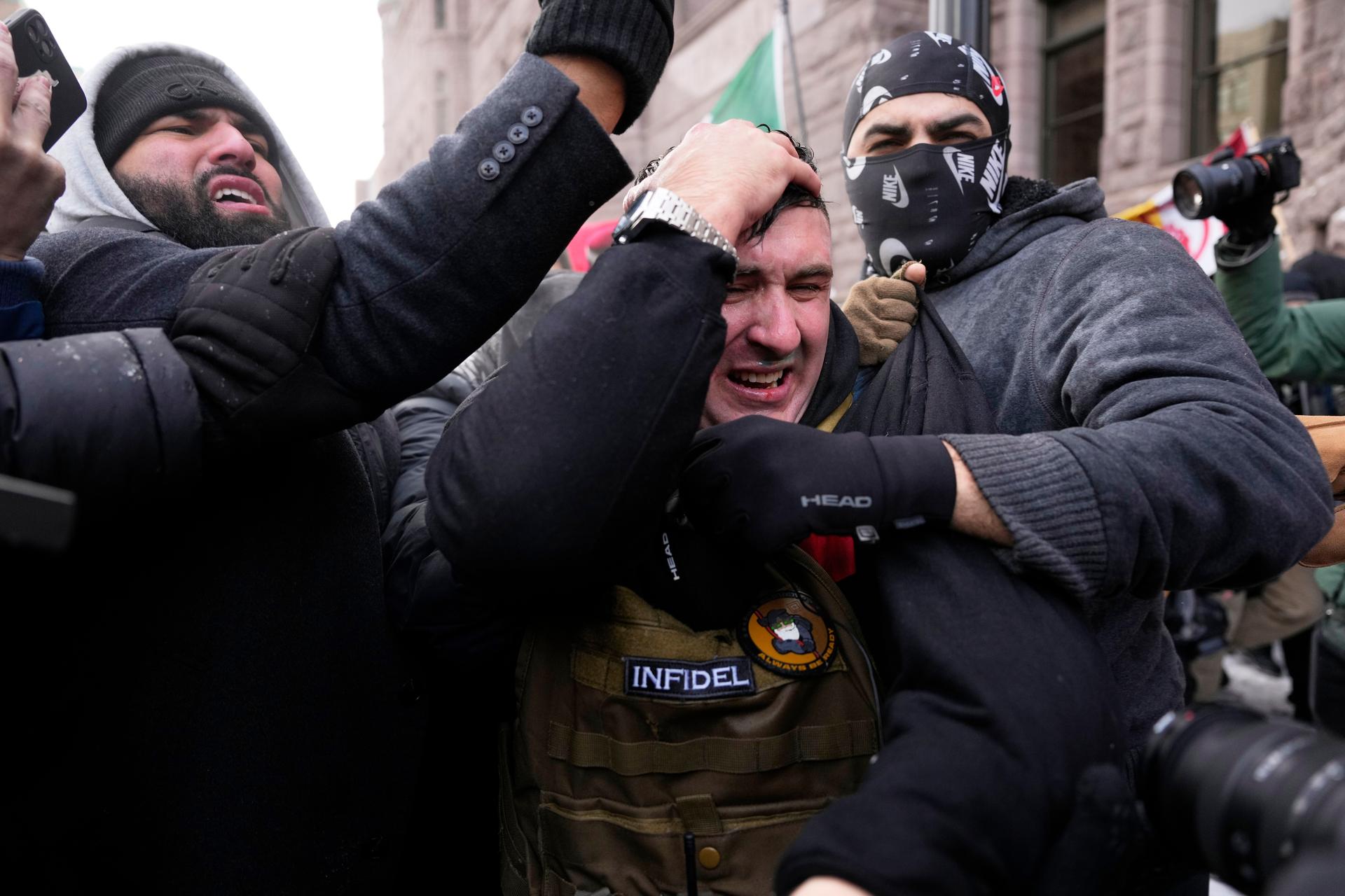 Jake Lang, center, who organized the protest March Against Minnesota Fraud, clutches his head as he leaves the rally near Minneapolis City Hall on Saturday. (AP Photo/Yuki Iwamura)