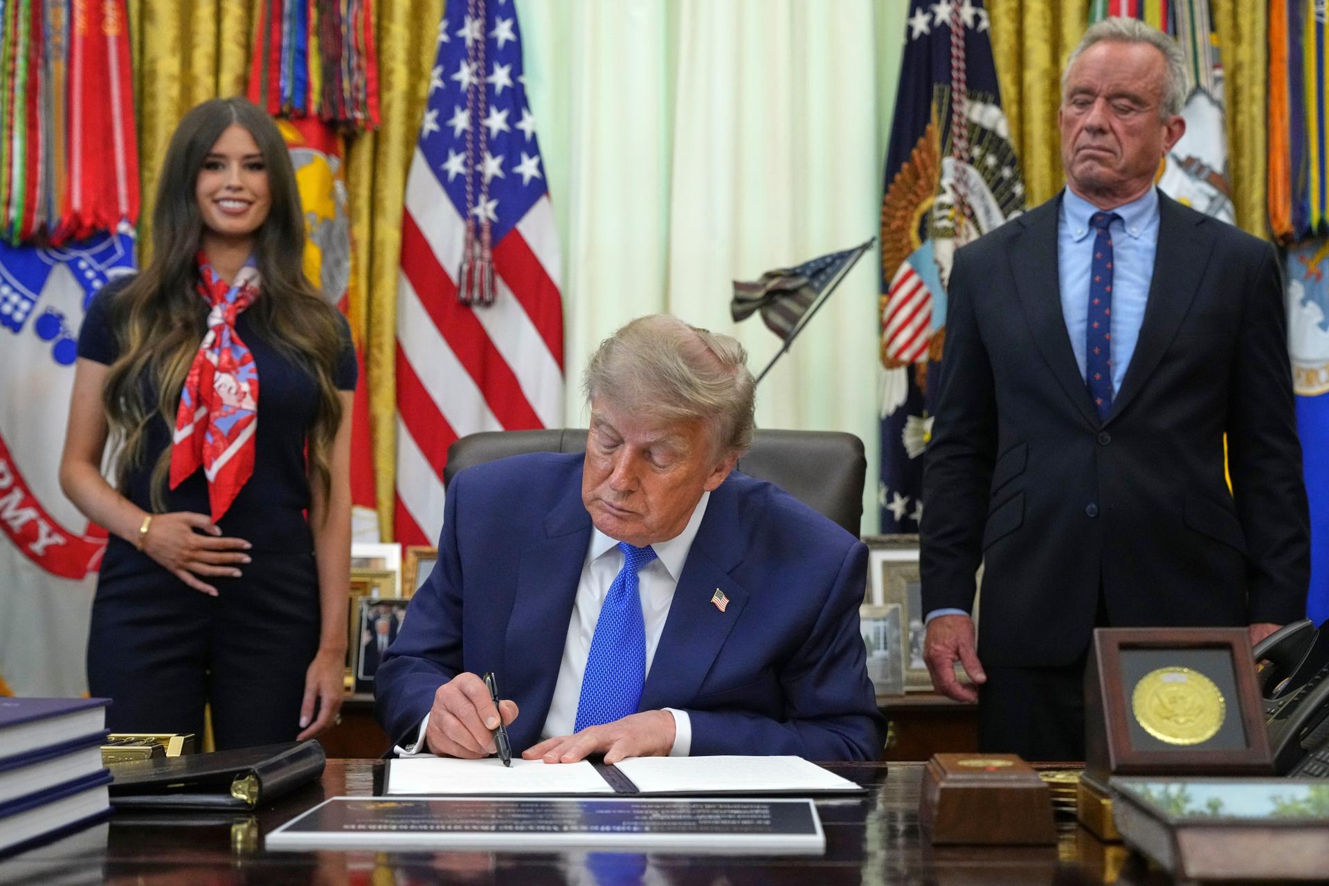 President Donald Trump signs an executive order as Jayme Franklin, left, and Health and Human Services Secretary Robert F. Kennedy Jr. watch Monday, in the Oval Office of the White House in Washington. 
