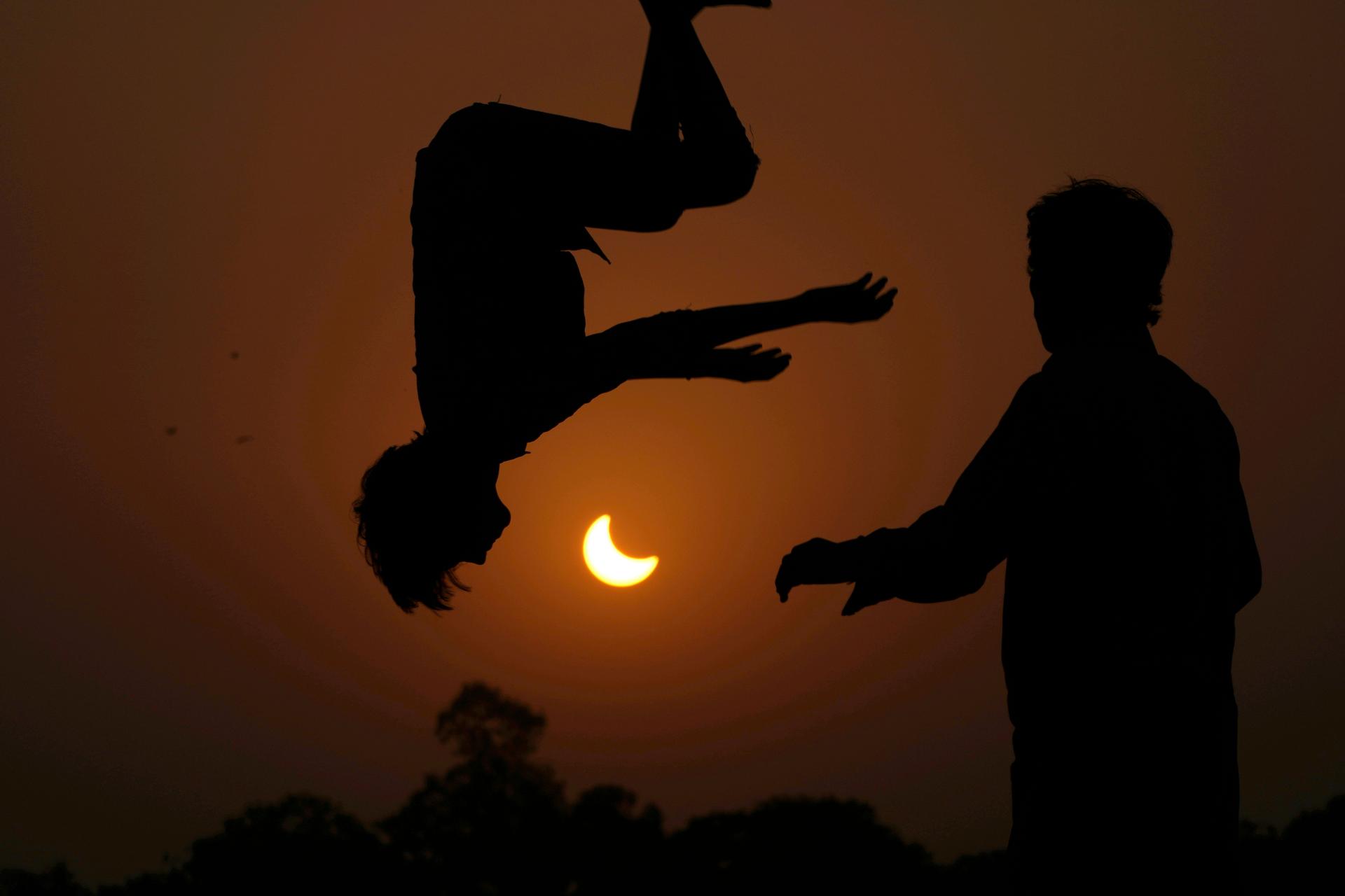 The partial solar eclipse is framed by youngsters jumping on a trampoline in the outskirts of Lahore, Pakistan, 2022. 