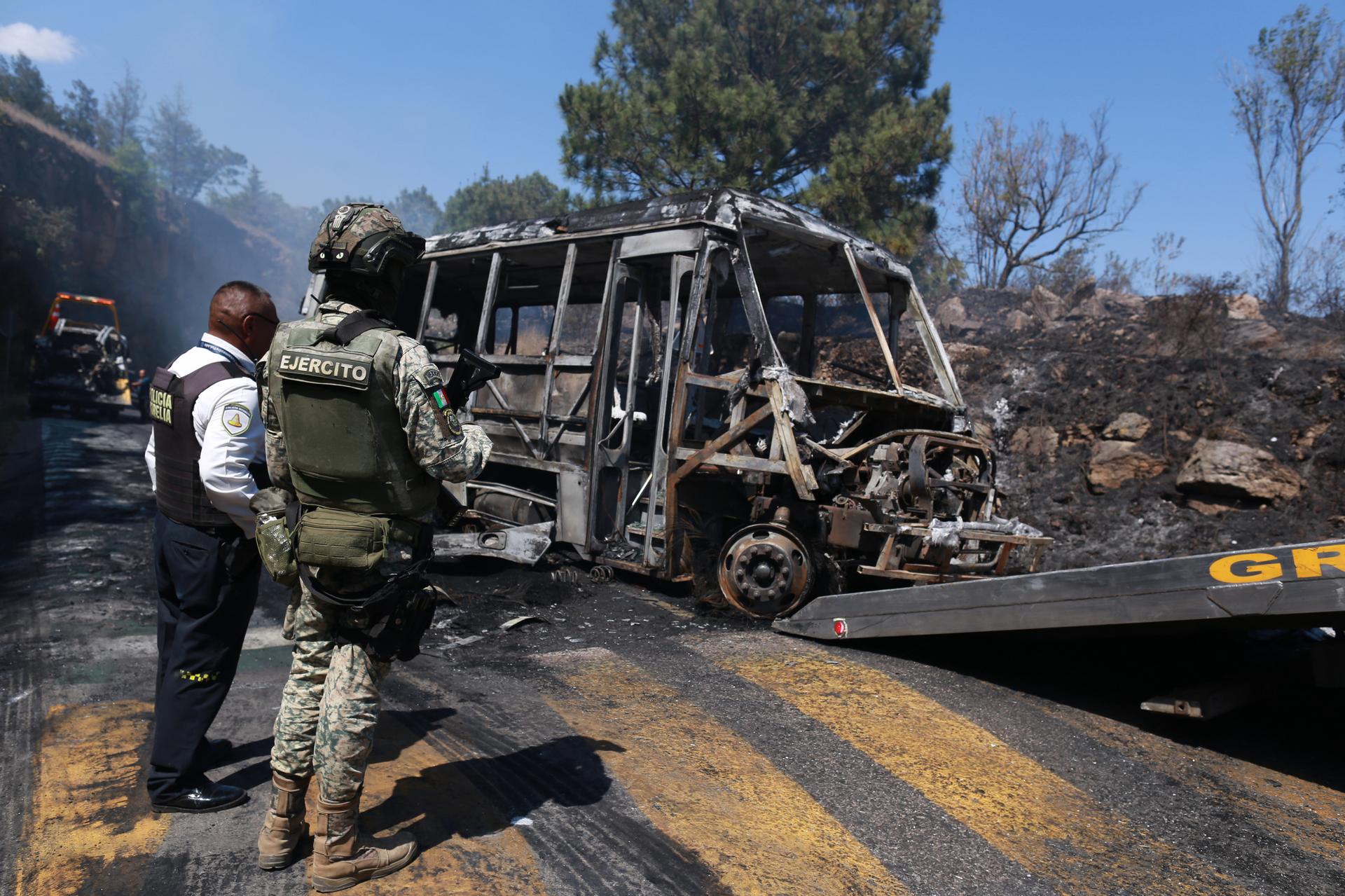 A soldier stands guard by a charred vehicle that was set on fire in Cointzio, Mexico, Sunday, amid reports the Mexican Army killed the Jalisco New Generation Cartel leader known as 
