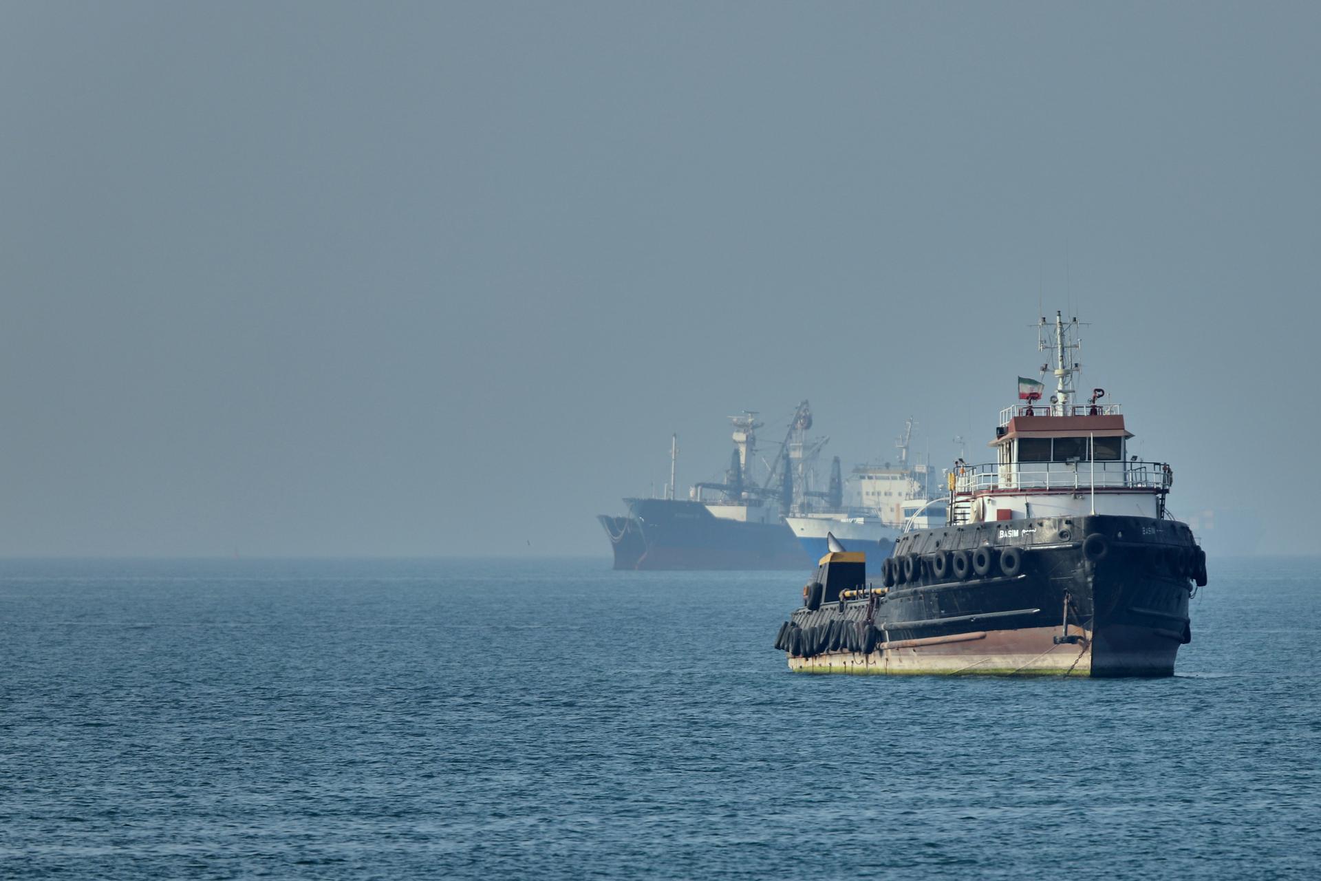 An Iranian tugboat floats in the foreground as cargo ships sit at anchor in the Strait of Hormuz off Bandar Abbas, Iran, on Monday. (Amirhosein Khorgooi/ISNA via AP)