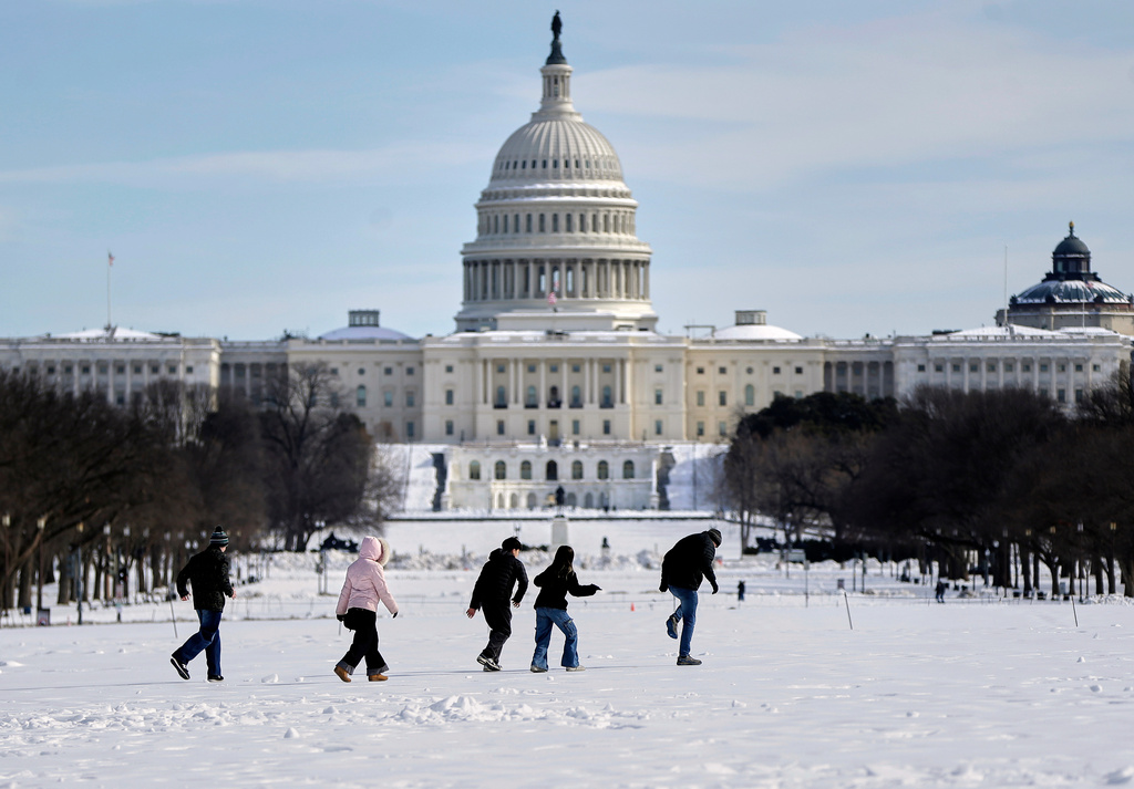 This is a picture of the U.S. Capitol in Washington, D.C., as people walk in front of the complex through the snow.