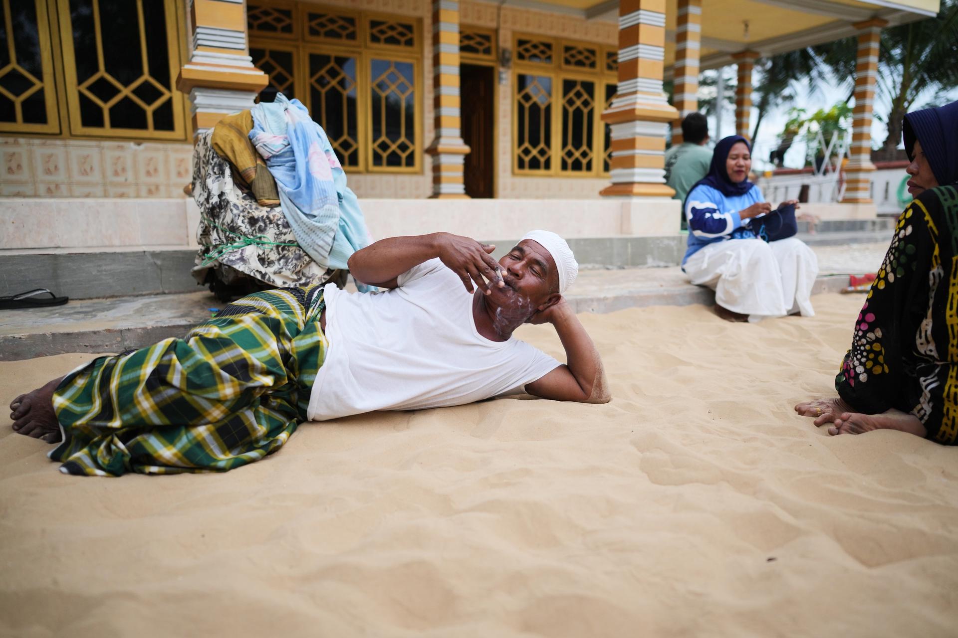 Adnan, who goes by one name only, smokes a cigarette as he lies on sand in Legung Timur village in Sumenep on Madura Island, Indonesia.