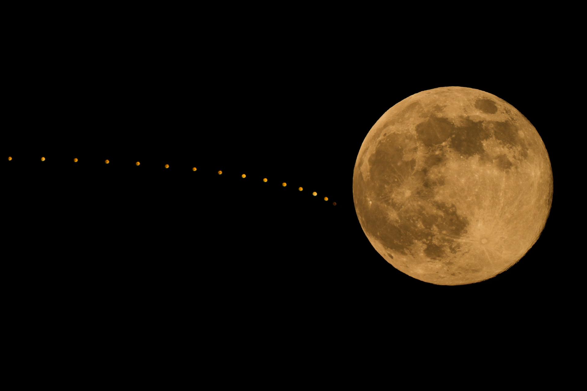 The full supermoon rises beyond lights atop a hotel, Thursday, in Kansas City, Mo.