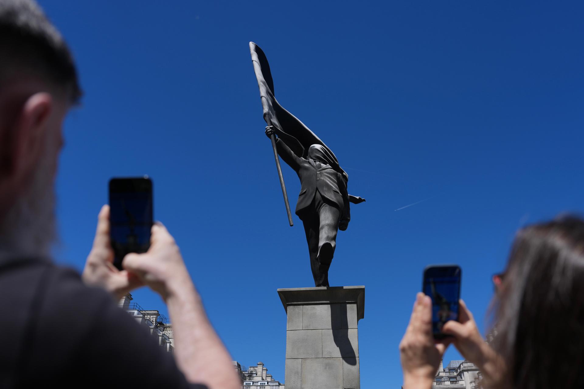Members of the public look at a statue of a man holding a flag covering his face, and signed ‘Banksy’, which appeared in Waterloo Place in London on Thursday.
