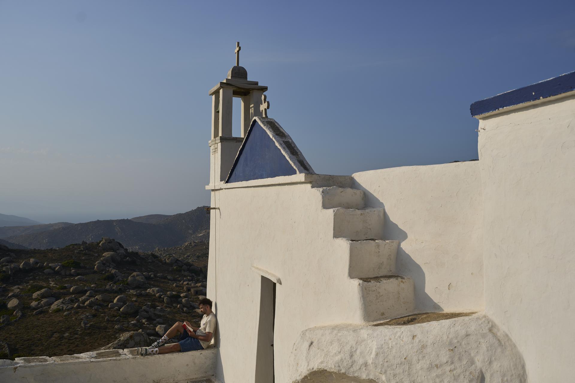Giannis Kafantaris 26, reads a book outside Panagia Theoskespasti, the chapel his family co-owns near the village of Falatados on Sept. 5. (AP Photo/Petros Giannakouris).