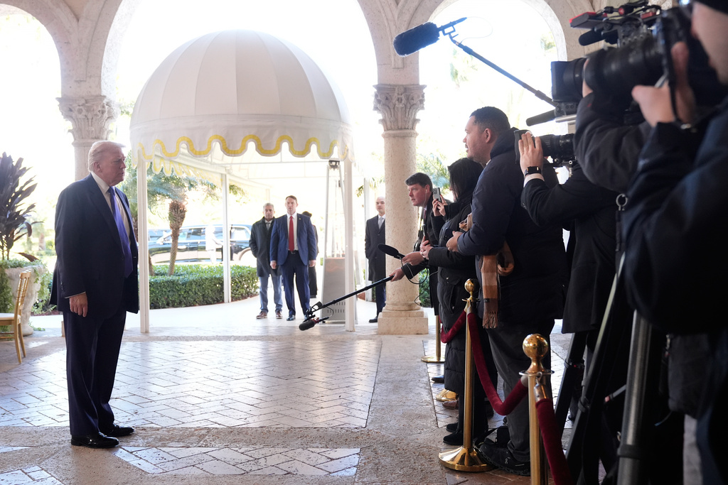 This is a picture of President Donald Trump standing on the left as he talks with reporters gathered at his Mar-a-Lago club.