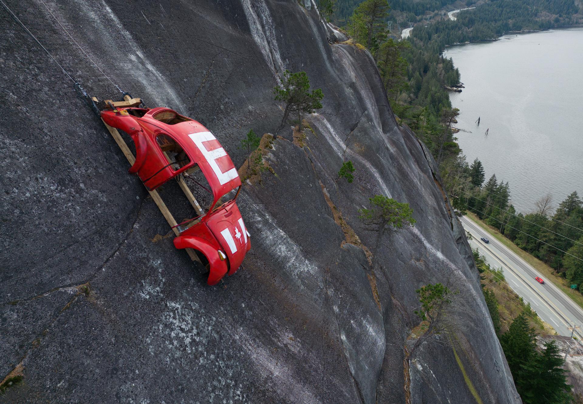 The shell of a Volkswagen Beetle hangs suspended on a cliff above the Sea-to-Sky Highway, in Squamish, British Columbia, Monday, after it appeared on the rock face last week with a large 