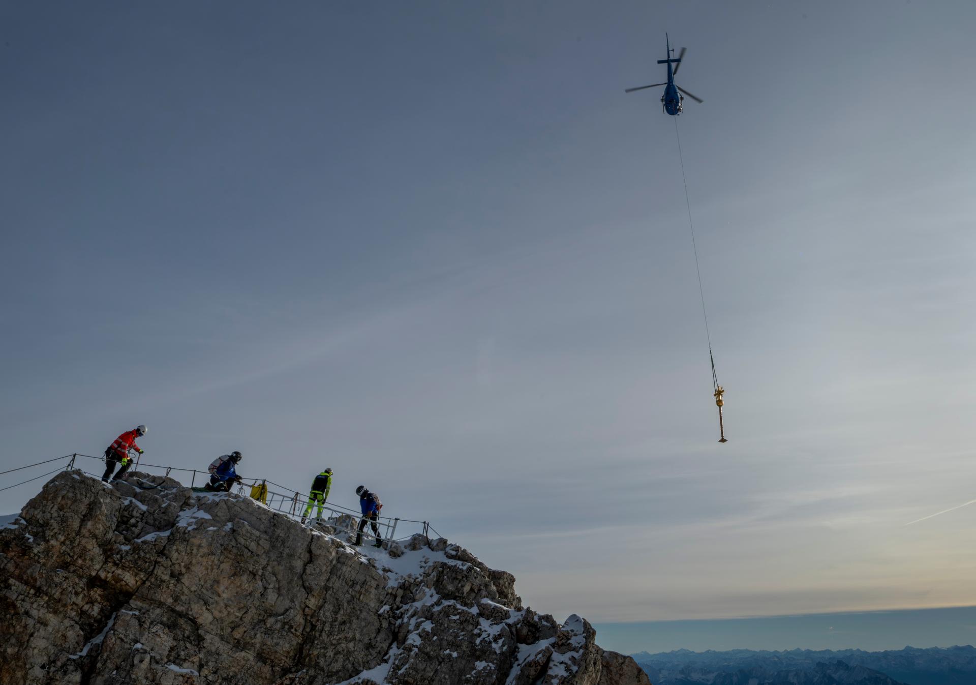 The gilded summit cross on the peak of the Zugspitze is flown across the valley by helicopter for restoration on Tuesday. (Peter Kneffel/dpa via AP)