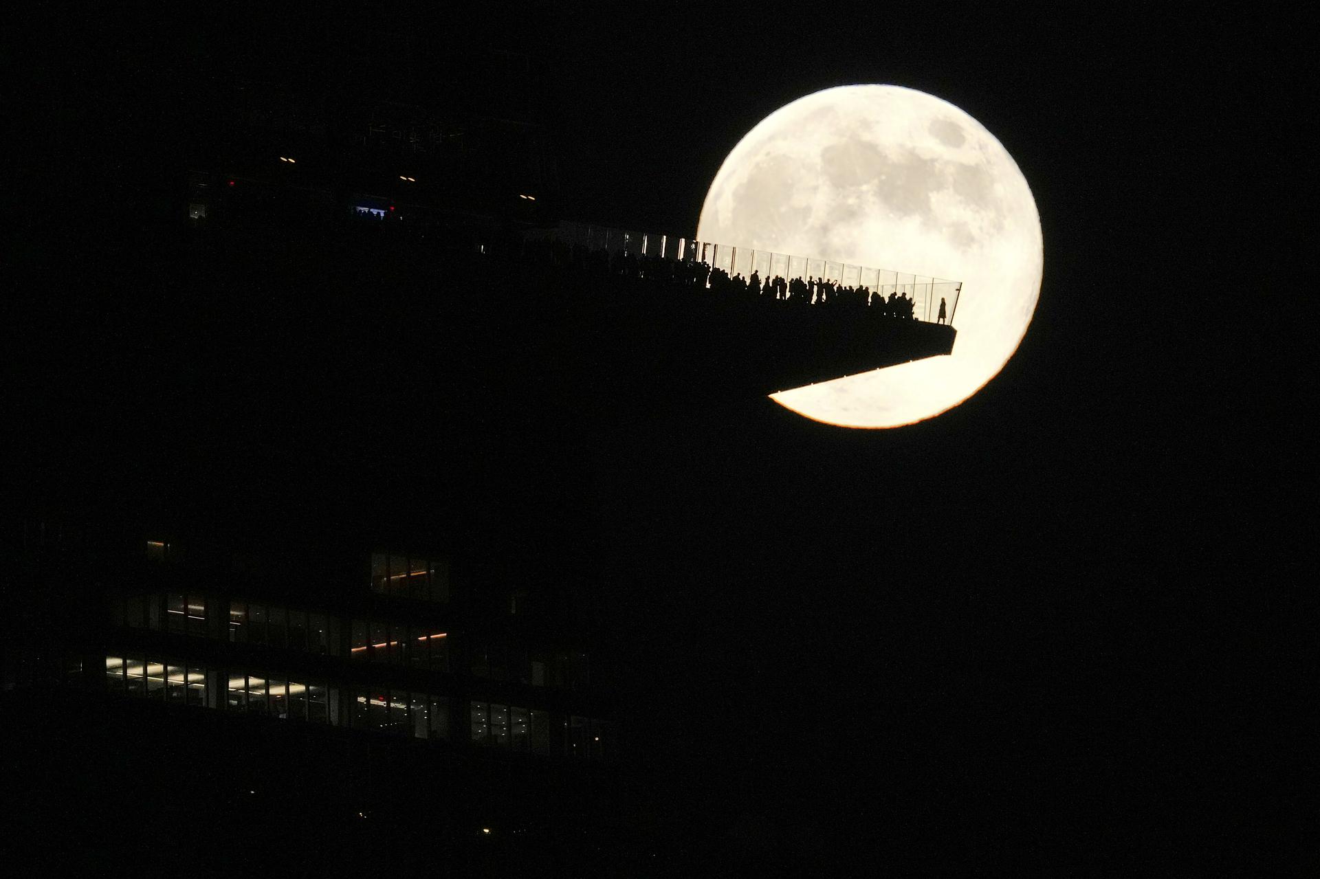 The moon rises behind an observation deck in New York City as seen from Hoboken, N.J., on Nov. 2024.