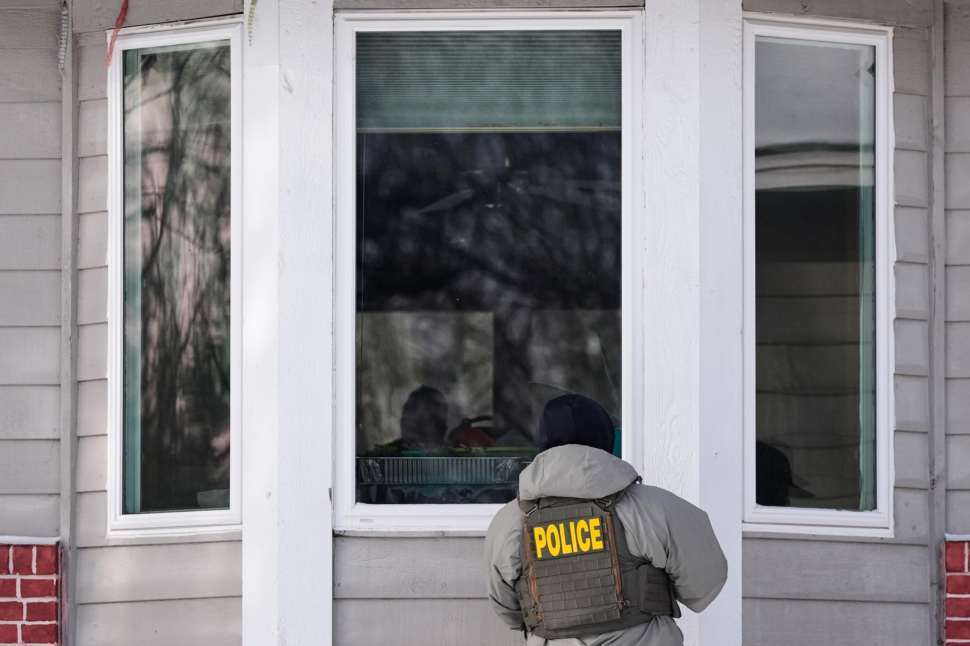 A federal immigration officer looks through a window of a home in Maplewood, Minn., on Tuesday. (AP Photo/Yuki Iwamura)