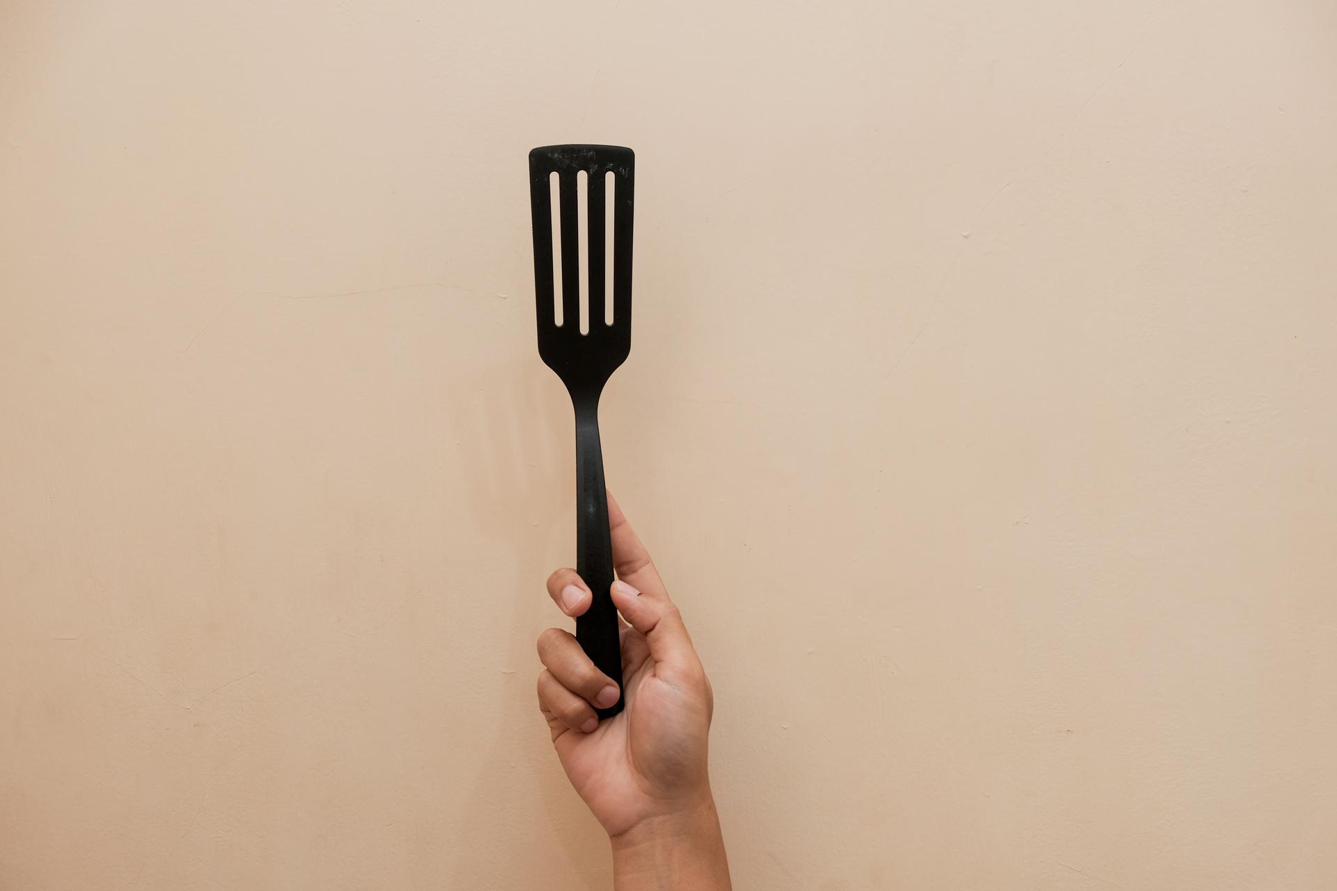 A hand holding a black spatula.