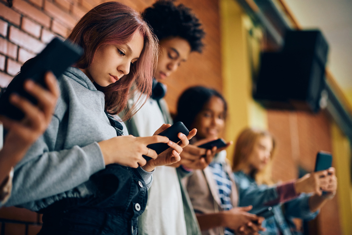 A line of children standing in a school hallway with smartphones in their hands.