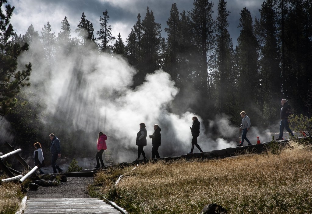Tourists walk past steam from hot springs at Yellowstone National Park.