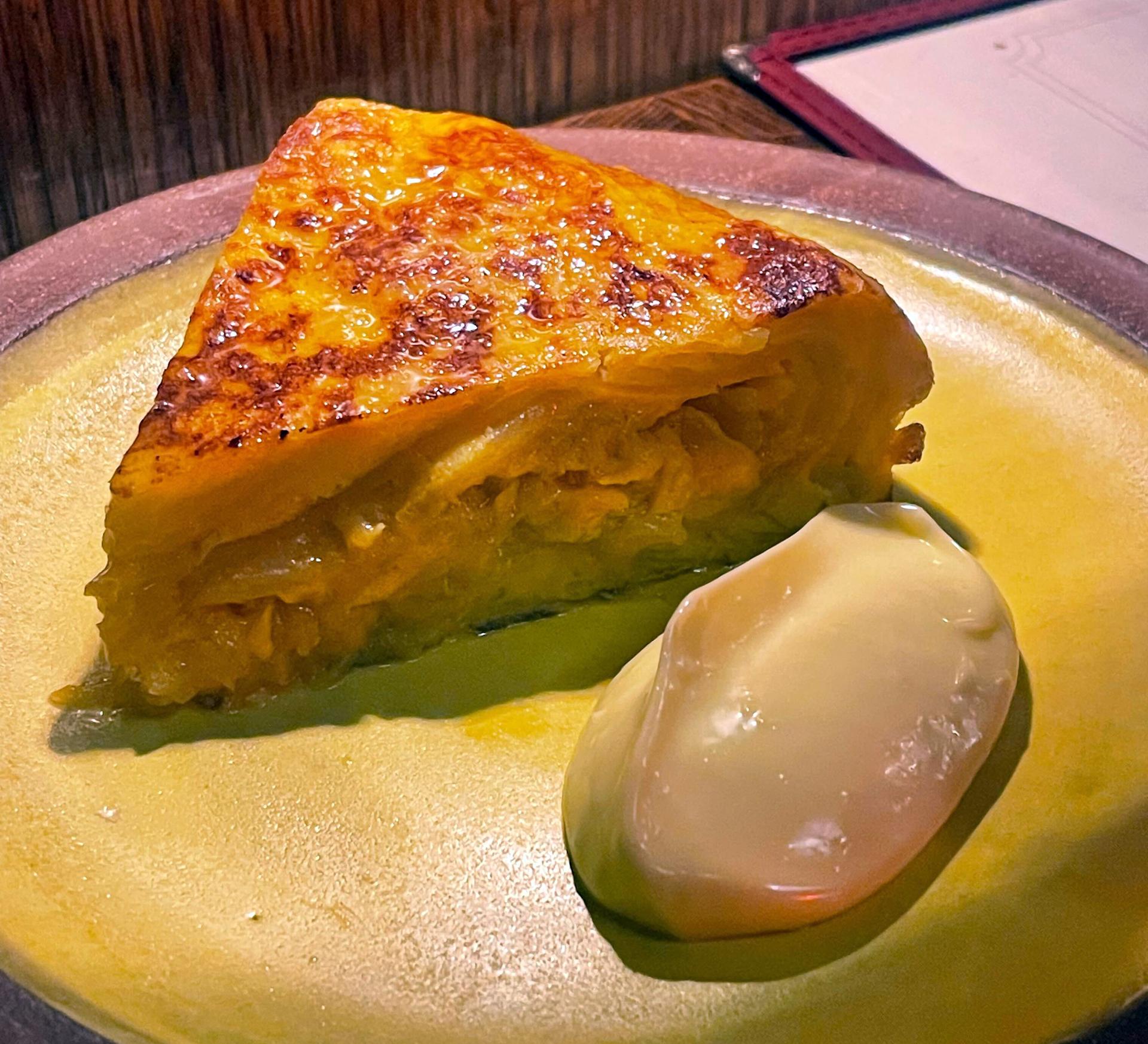 A slice of a thick potato tortilla next to a clump of sauce. 