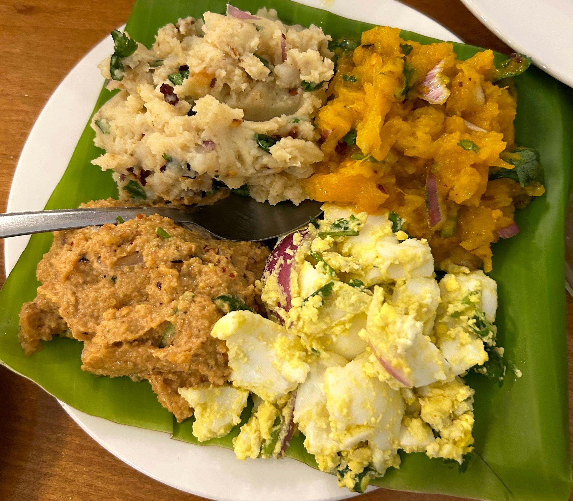 A plate with a big green leaf on it topped with four different smushed foods.