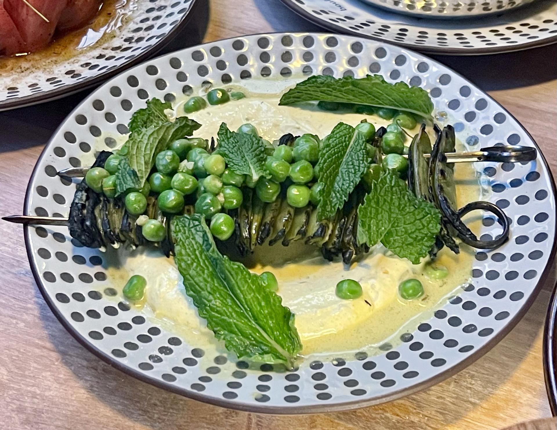 A skewer ona plate with peas and green mint leaves and creamy yogurt.