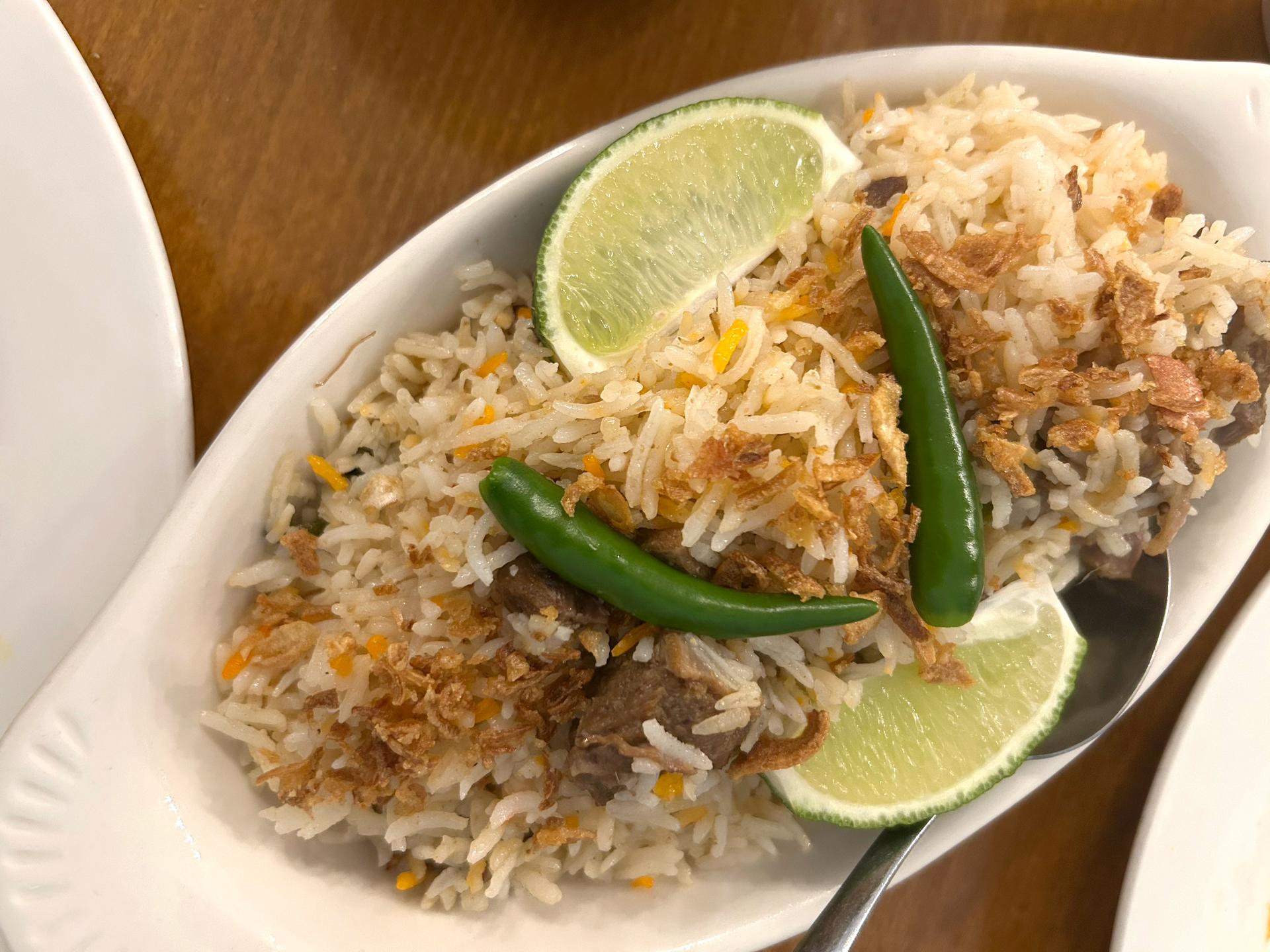 A plate of rice with crispies and green chile peppers and lime wedges.