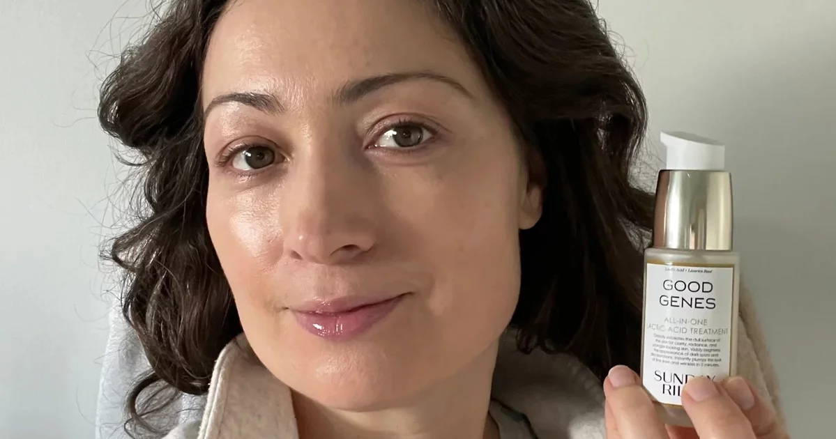 A brunette woman holding Sunday Riley's Good Genes Product