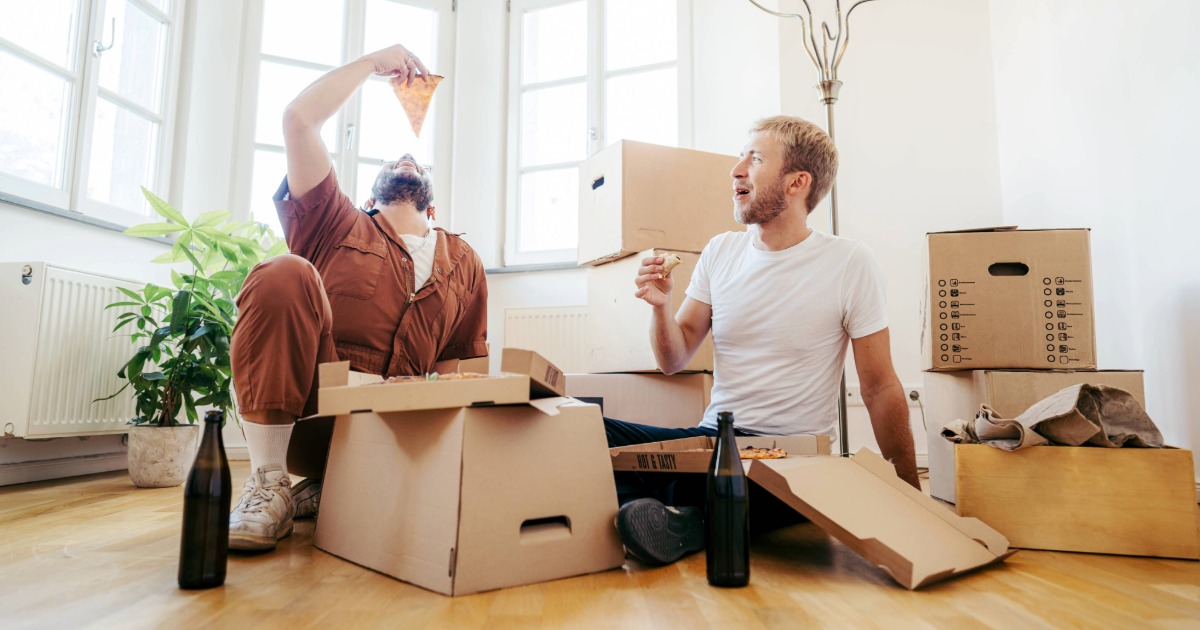 Two people eating pizza in apartment with moving boxes