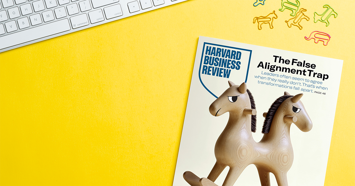 A Harvard Business Review magazine on a yellow surface, featuring two wooden horse figures. A keyboard is in the top left, with playful animal-shaped paperclips nearby.