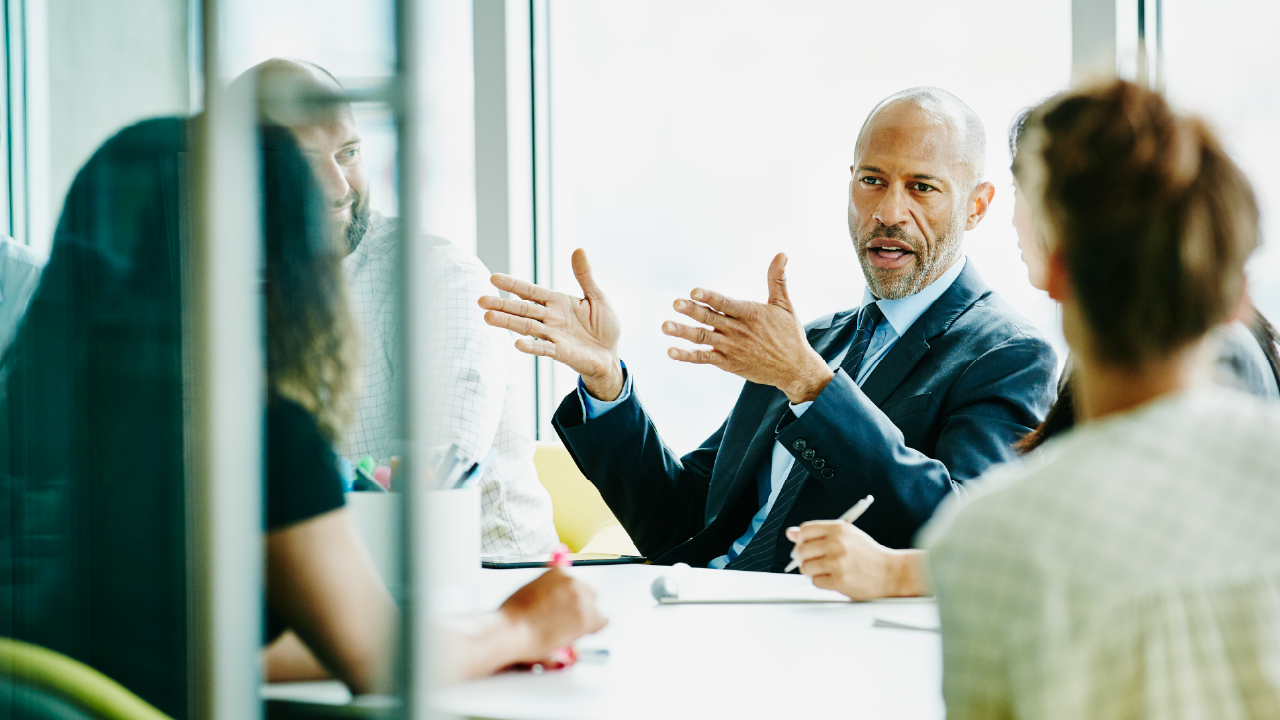 A business professional speaking with colleagues during a meeting.