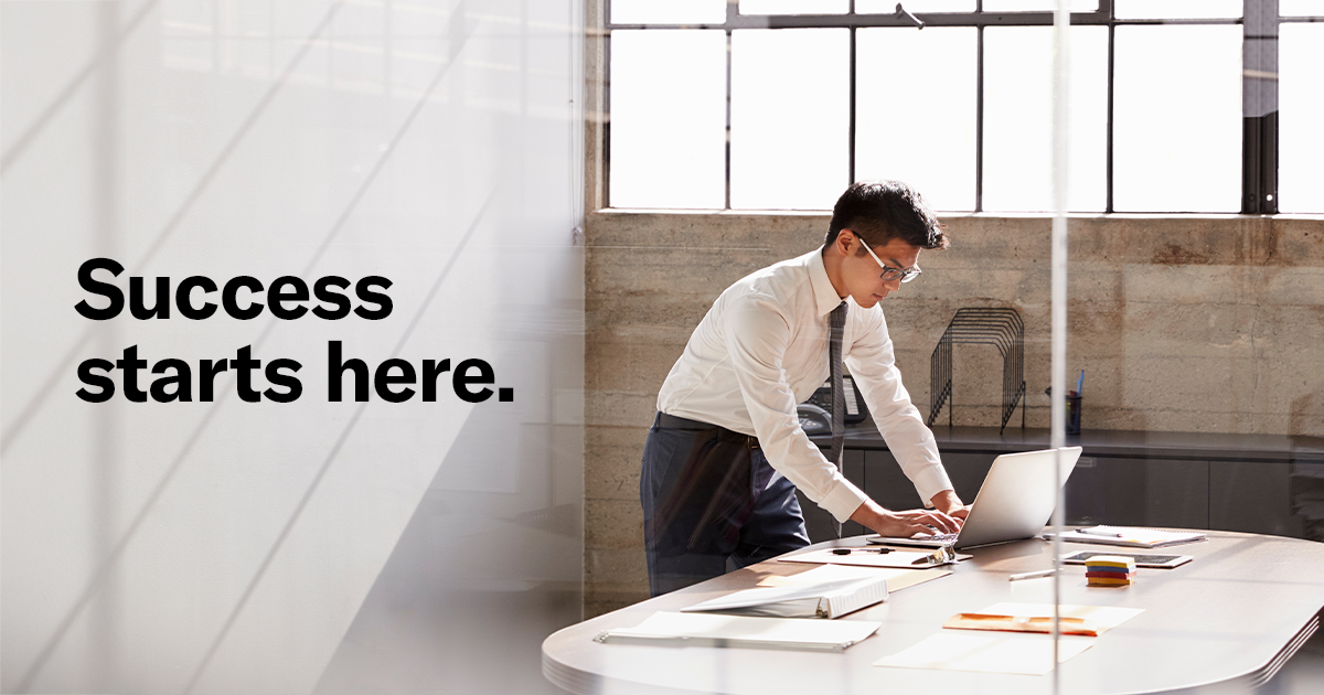 Man in office attire working on a laptop at a modern, sunlit desk. Text on the left reads 'Success starts here,' conveying motivation and focus.