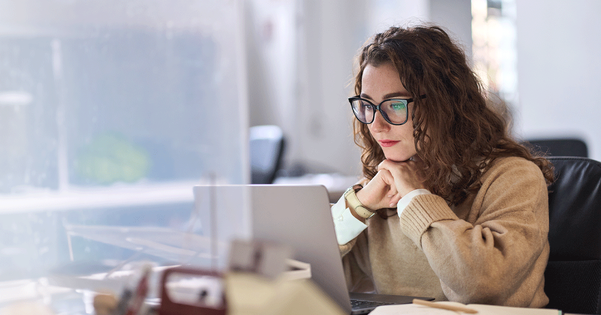 Person wearing glasses working on a laptop at a desk.