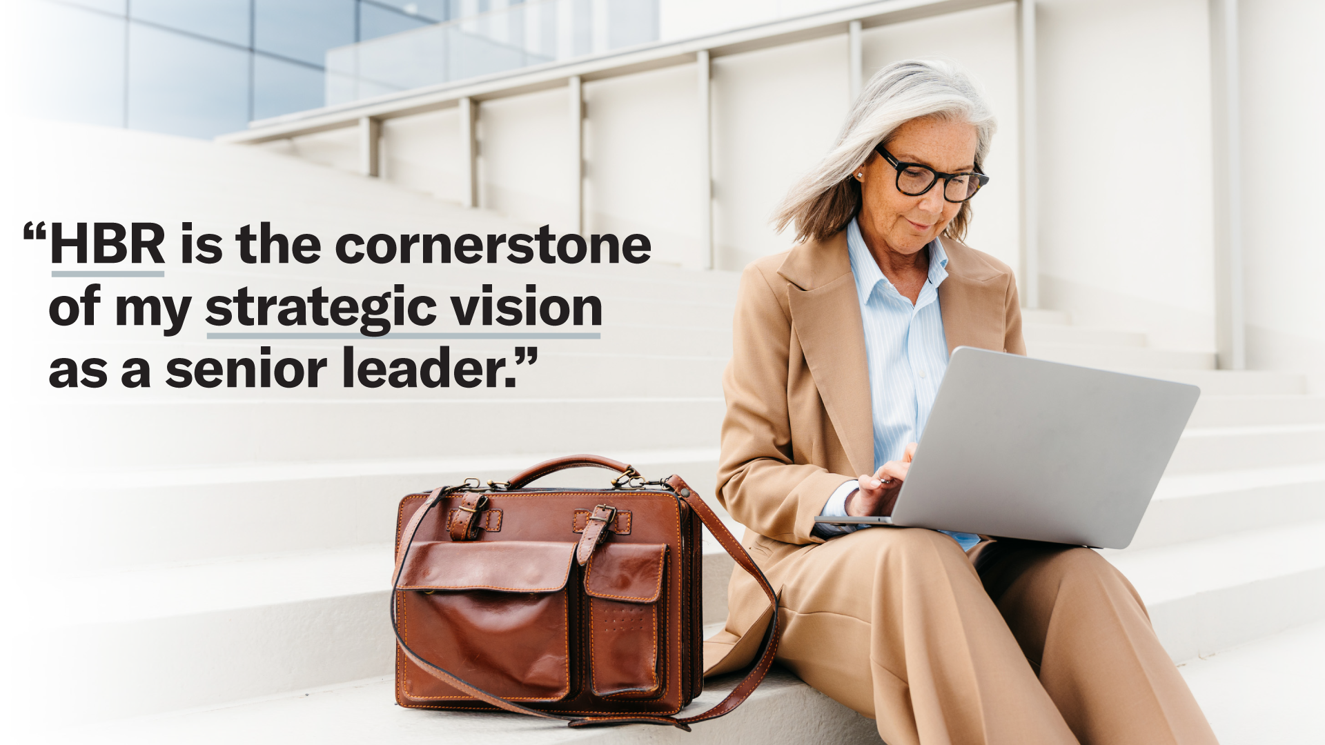 Person working on a laptop while seated on steps, alongside the testimonial: ‘HBR is the cornerstone of my strategic vision as a senior leader.’