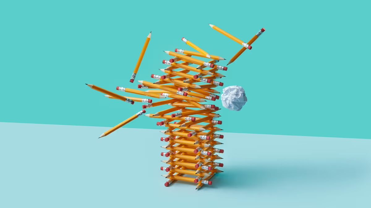 An image of pencils stacked like a tower that’s being hit by a ball of paper