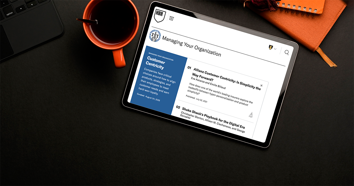A tablet displays Harvard Business Review case selections on customer centricity, featuring articles and case studies about customer-focused business strategies. An orange coffee mug and notebook sit nearby on a dark desk.
