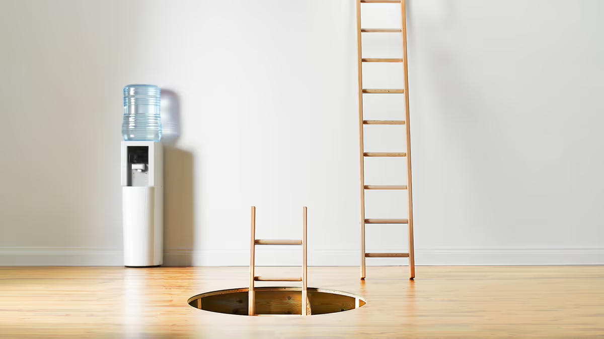 A picture of an empty room with a water cooler and a ladder with a hole in the floor and a ladder coming through.
