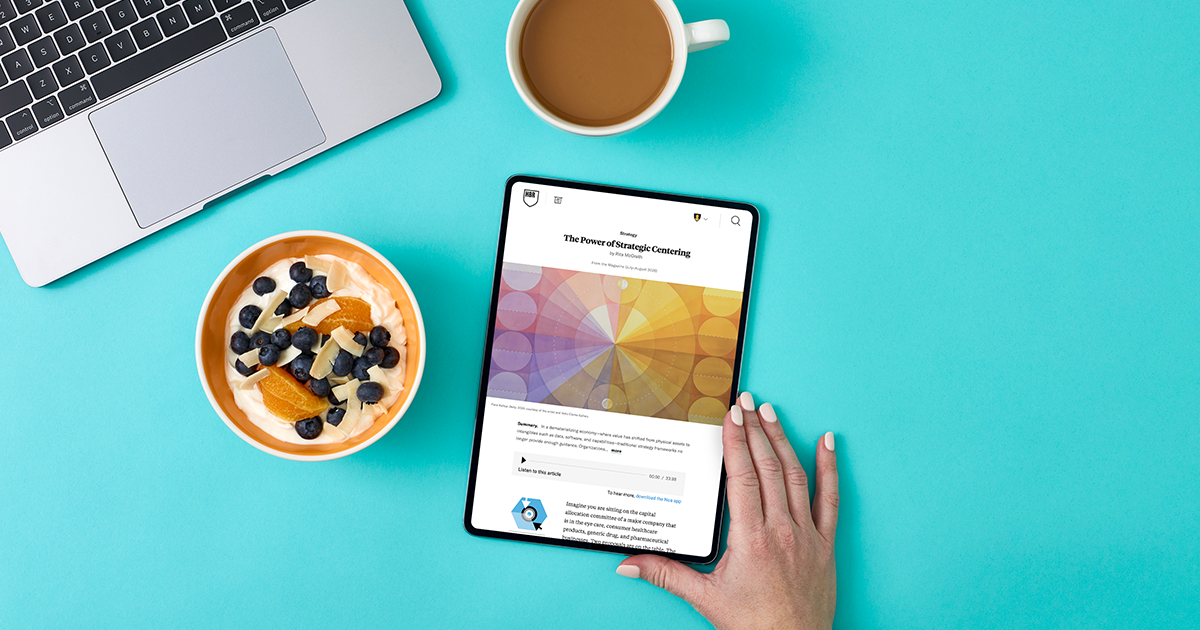 Tablet displaying an HBR article beside coffee and breakfast on a turquoise desk.