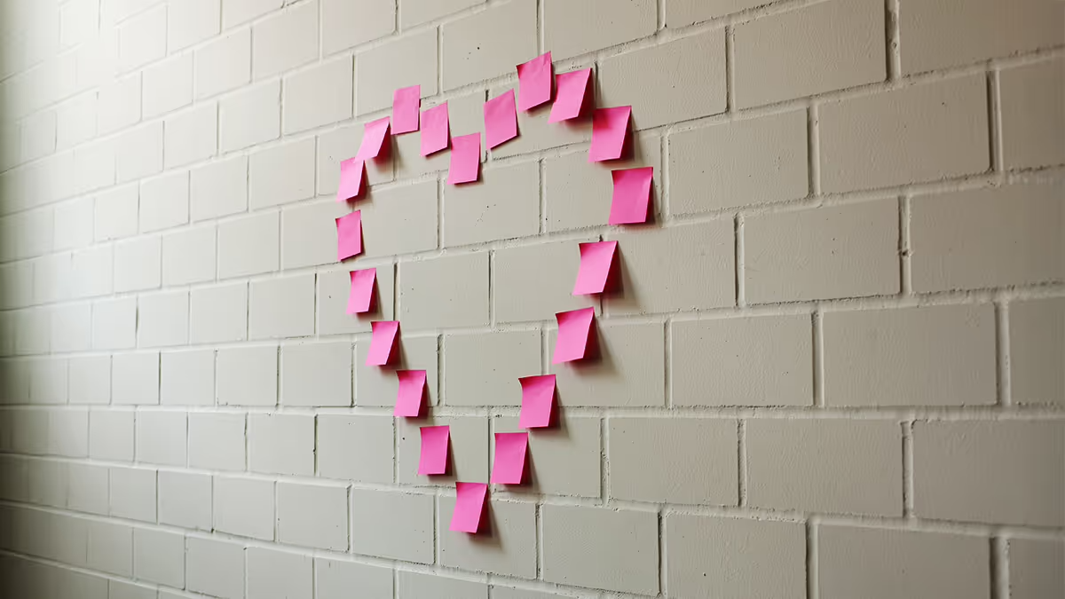 A photo of a wall with a heart made up of pink post it notes.