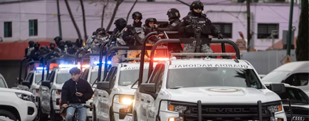 A line of white military trucks, with troops in dark uniforms standing in the truck beds, outside a building A line of white military trucks, with troops in dark uniforms standing in the truck beds, outside a building