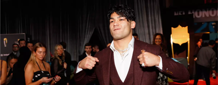 Puka Nacua in a three-piece suit with a white shirt and no tie holds his fists up by his lapels