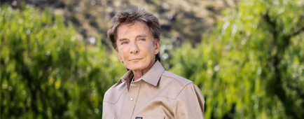 Barry Manilow, wearing a khaki shirt and brown pants, stands on his lawn.