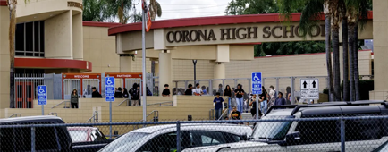  A parking lot is in front of young people standing near and under a building sign that says 