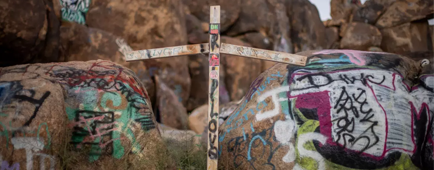 A wooden cross stands next to boulders covered in graffiti at the location where Lorraine Bird's body was found.