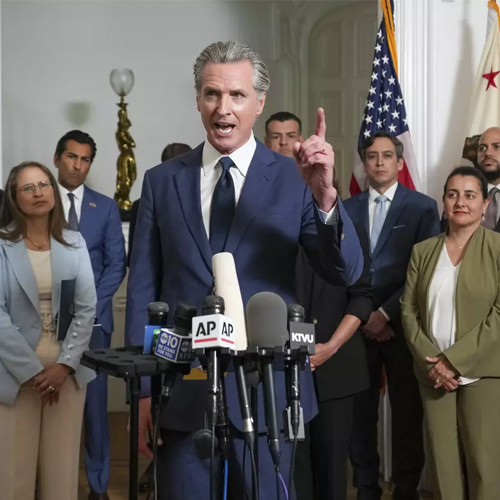 A man speaks at a lectern while people stand behind him.