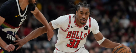 A man in a Chicago Bulls uniform bends down while dribbling the ball, using his right arm to fend off a defender A man in a Chicago Bulls uniform bends down while dribbling the ball, using his right arm to fend off a defender