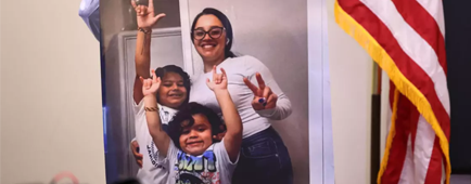 A large photo of two smiling children and a woman with a ponytail and glasses smiling.