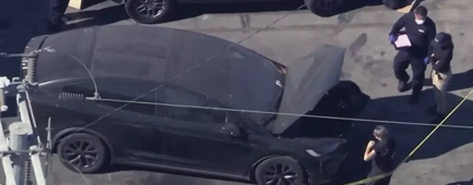 Police examine the trunk of a black Tesla.