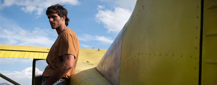 A man leans against a yellow prop plane.