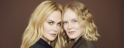 A woman in a navy suit embraces a woman in a brown suit as they both look to the side.