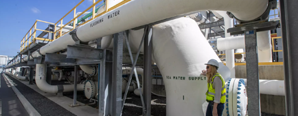 A person stands by large water pipes at a desalination plant. A person stands by large water pipes at a desalination plant.