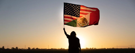 A silhouetted figure raises a combination United States and Mexico flag.